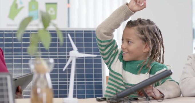 Teacher asking in class child in green-top raising hand, testing tablet and module near solar panel
