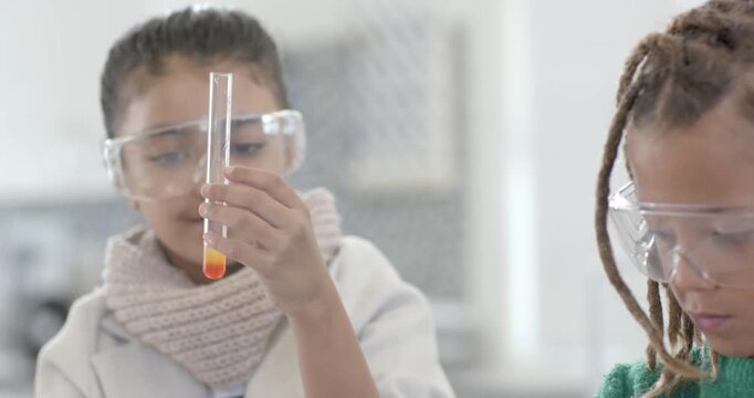 Teen girls wearing goggles at lab after teacher smile, inspecting test tubes observing orange layer