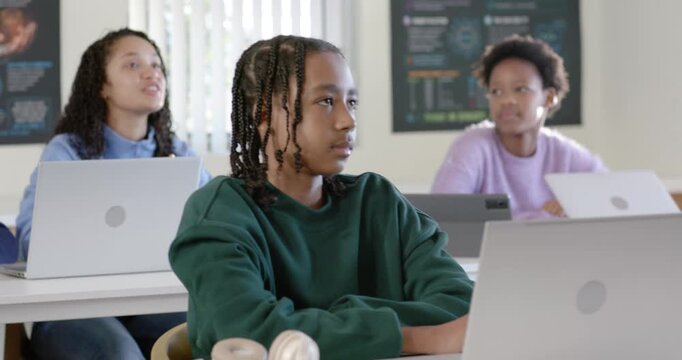 Class watching teacher talking, African American teen typing on laptop headset in class, copy space