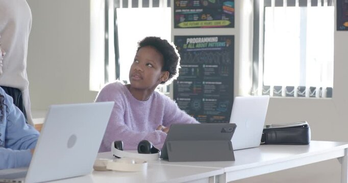 African American female teens using laptops looking up in lab while Indian teacher walking to help