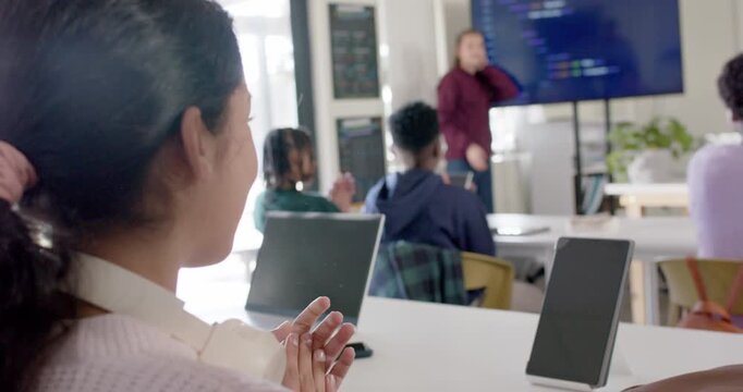 Diverse teens clapping then watching maroon-clad presenter finishing coding on display in classroom