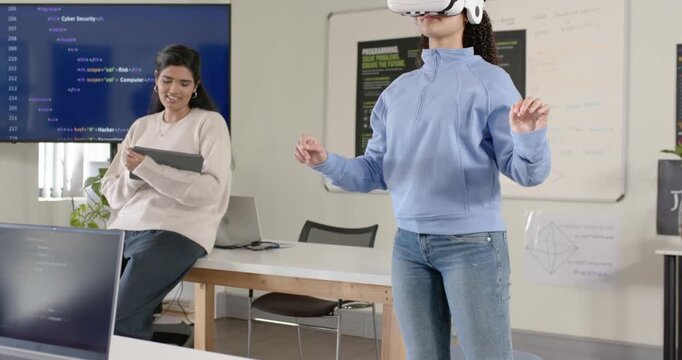 Female developers working in lab, one holding tablet while other activating white VR, testing demo