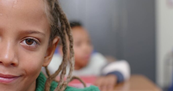 African American teenage pupil noticing lens opening eye smiling in green top at desk, copy space