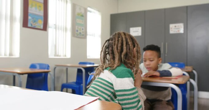 African American school boys, front boy noticing peer writing at desks, leaning and offering pencil