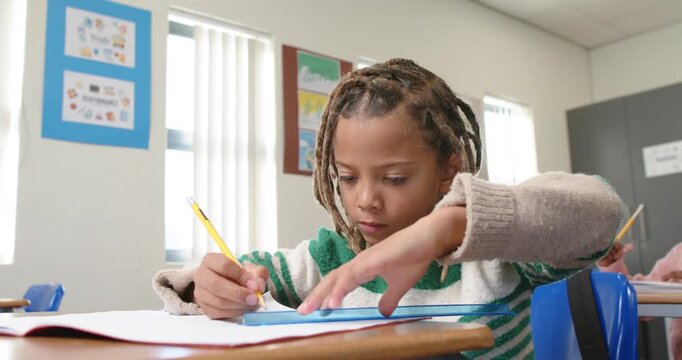 African American child starting work writing with yellow pencil using blue ruler in classroom