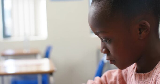 African American child looking down, studying worksheet at school desk in pink sweater, copy space