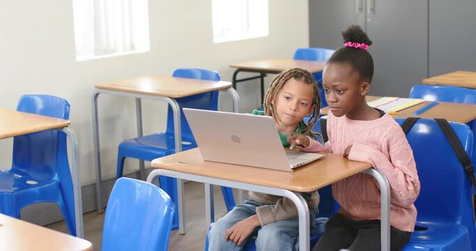 Diverse students seeing laptop content, collaborating at desk, girl using trackpad, boy peering