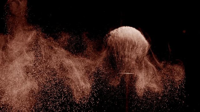 Macro slow-motion shot of black brush flicking beige powder against a dark backdrop | Concept for bronzer commercial