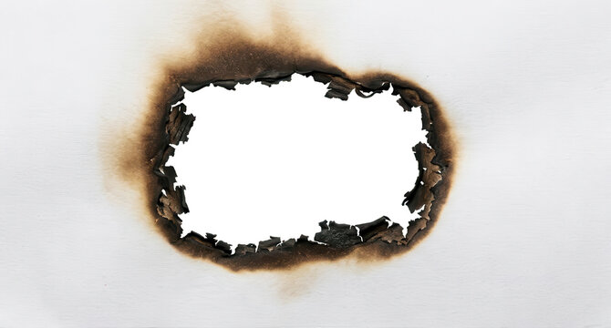 A close up view of a white paper sheet with a large burn hole in the center showing charred edges and dark scorched smoke stains spreading across the textured surface burned paper