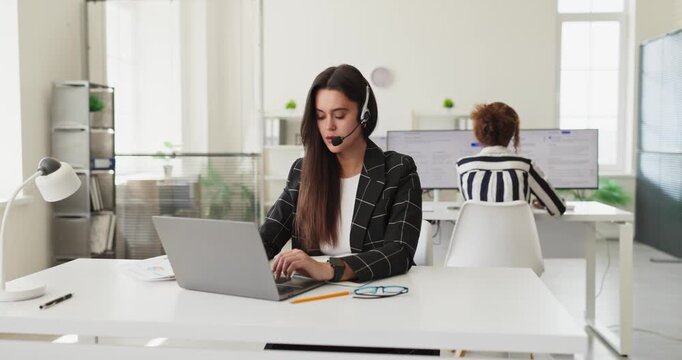 Operator woman with headset microphone handling call. At a computer in a bright office, she offers support and consultation to clients. Concept shows efficient customer service workflow.