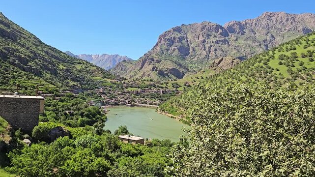 Calm green river winds through a sun-drenched mountain village, framed by terraced orchards and rugged spring peaks under a clear blue sky.
📍Selin village, Hawraman Takht, Kurdistan 