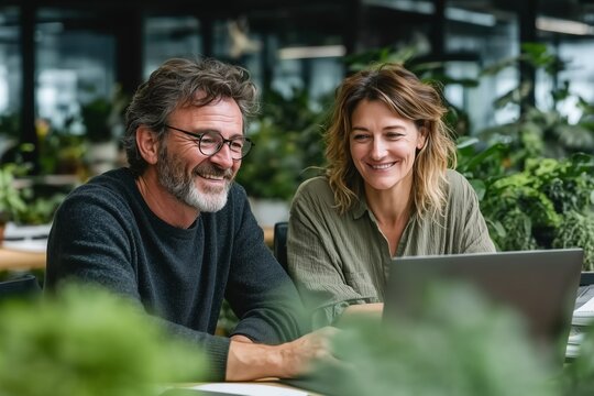 Smiling middle-aged colleagues working together on a laptop in a modern office