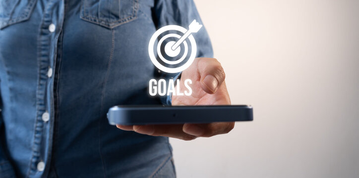 Hand holds tablet displaying a target icon with the word "GOALS"
