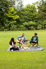 GrandFather playing acoustic guitar for child during picnic. Asian family enjoy outdoor picnic with...