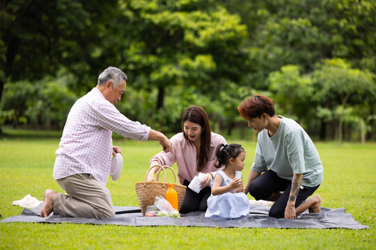 Happy Asian family having fun time on picnic at city nature park sunny day, outdoor activitie with daughter father, mother and grandfather