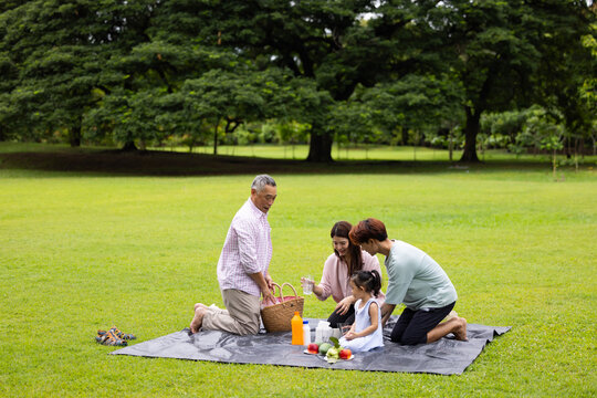 Happy Asian family having fun time on picnic at city nature park sunny day, outdoor activitie with daughter father, mother and grandfather