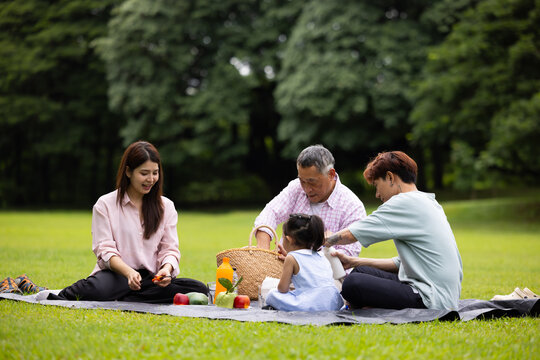 Happy Asian family having fun time on picnic at city nature park sunny day, outdoor activitie with daughter father, mother and grandfather