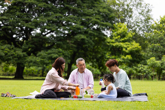 Happy Asian family having fun time on picnic at city nature park sunny day, outdoor activitie with daughter father, mother and grandfather