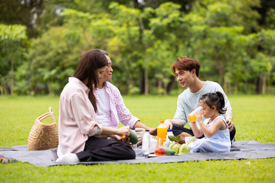 Happy Asian family having fun time on picnic at city nature park sunny day, outdoor activitie with daughter father, mother and grandfather