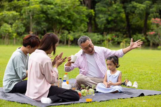Happy Asian family having fun time on picnic at city nature park sunny day, outdoor activitie with daughter father, mother and grandfather
