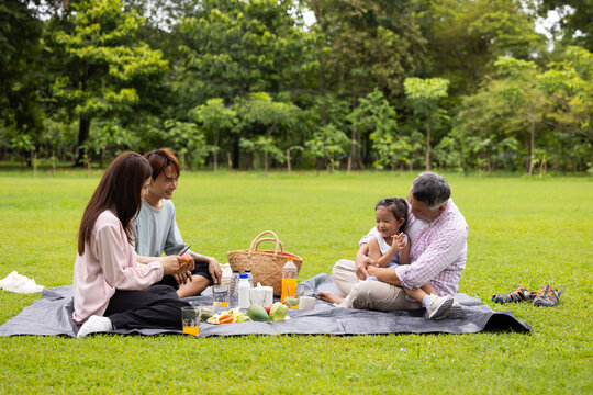 Happy Asian family having fun time on picnic at city nature park sunny day, outdoor activitie with daughter father, mother and grandfather
