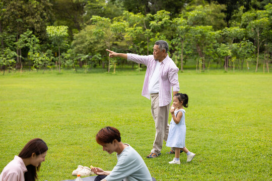 Little girl walking and spending time with grandfather in the park. Happy Asian family having fun time on picnic at city nature park, outdoor activitie