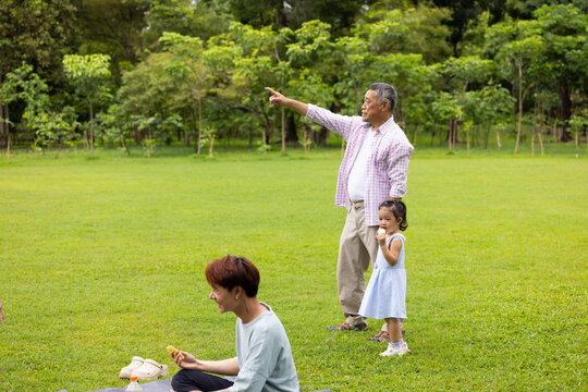 Little girl walking and spending time with grandfather in the park. Happy Asian family having fun time on picnic at city nature park, outdoor activitie