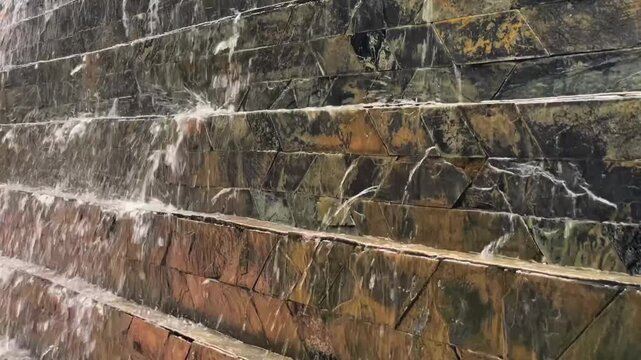 A close-up of a stream of water flowing down a cascading natural stone wall. A decorative water feature for landscape design, architecture, and tranquil ambiance.