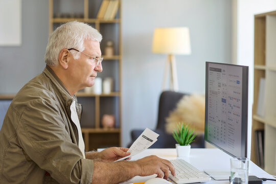 Senior man bills payment invoice with calculator. At a home computer he reviews utilities, tracks expenses, and plans a monthly budget. Concept of personal household finance and budgeting.