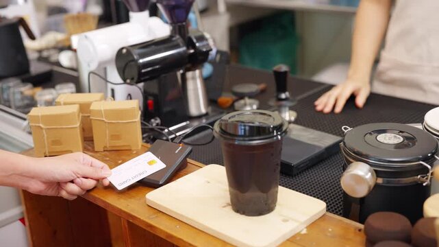 Credit card payment at coffee shop counter. Cafe owner using card reader for cashless transaction while serving coffee drink to customer. Electronic payment technology for small business retail store.