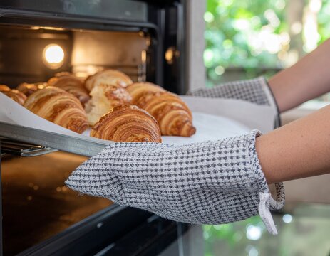 Person taking a tray of freshly baked golden croissants out of the oven.