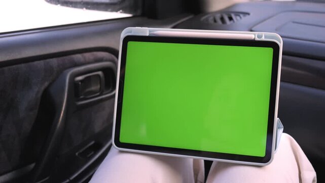 Hand interacts with a green screen tablet inside a car. The hand moves gently across the screen. The person appears calm and focused. Ideal for car tech or in-car entertainment content