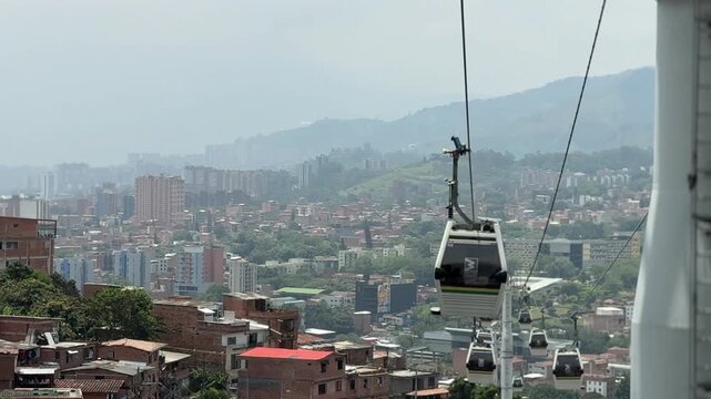 Multiple Metrocable gondolas suspended over hillside brick houses with the Medellin city skyline in the background