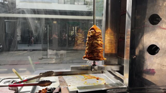 Shawarma Chicken Kebab on Vertical Rotisserie with Tools in Glass Case in street restaurant 