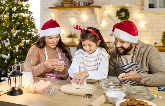 Christmas happy family baking cookies in cozy kitchen. Parents help child girl knead dough, cooking together in festive home. Winter holidays celebration, joy and togetherness concept.