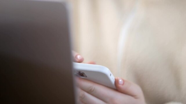 Close-up of hands using smartphone and laptop. Person focused on digital devices. Suitable for tech, multitasking, or modern work concepts