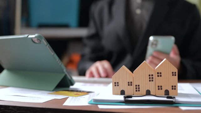 Real estate brokers analyze property investment market data, holding mobile phones near wooden house models, tablet computers, financial paperwork, credit cards, planning mortgage payment options.