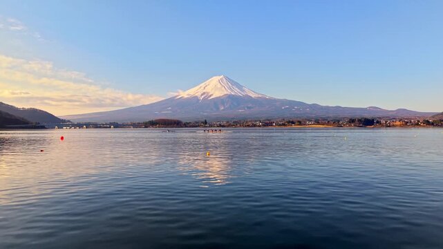 Rowing boat moving on a calm lake with mount fuji in the background on a sunny day.