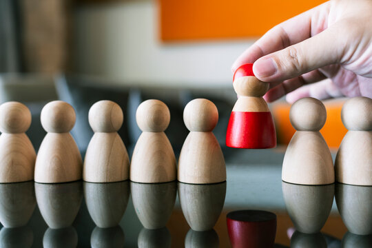 Hand choosing a red wooden figure from a row of plain figures. Concept of leadership, human resources recruitment, team management, and finding unique talent for business success.