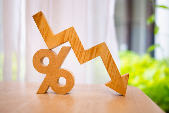 Wooden percentage sign with a falling down arrow graph. Concept of economic recession, interest rate decrease, inflation drop, financial loss, and market crash for business finance.