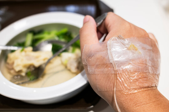 Patient hand with intravenous fluid drip tube resting near hospital food. Concept of healthcare, medical treatment, illness recovery, and clinical nutrition for healthcare industry.