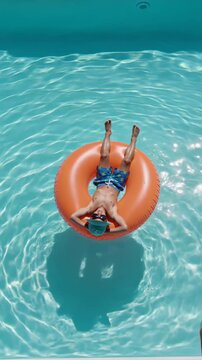 Aerial view of boy floating on orange inflatable ring in blue pool, vertical shot