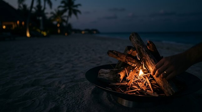 Hand lighting a small fire pit on a tropical beach at night