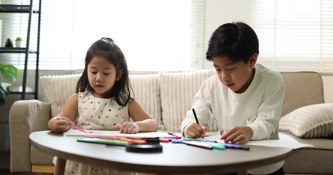 Asian mother remote working from home on a laptop in the living room while her two children are drawing and coloring at a low table, balancing work and family life