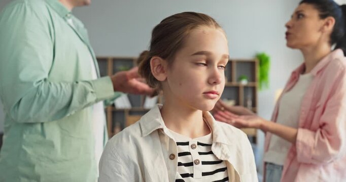 Child girl sees parents argument and conflict. She looks upset as mother and father quarrel in the background at home, reflecting stress, fear and tension. Clear concept of family conflict.