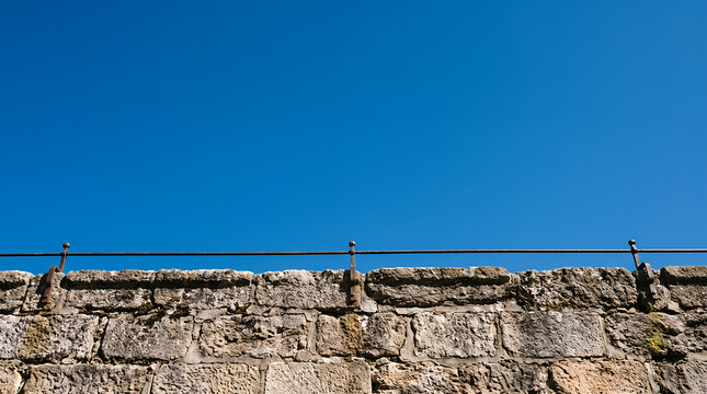 Old stone wall topped with a rusty iron railing under a vivid blue sky