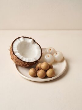 Fresh coconut halves, peeled lychees, and longan fruits arranged on a soft cream monochromatic background, realistic food photography, elegant composition, premium studio lighting, isolated fruits