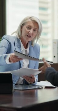 Businesswoman, talk and consultation in office with paperwork, finance advice or proposal for budget. Mature person, financial advisor and chat in meeting with documents, cost control plan or insight