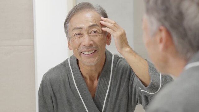 洗面所で髪の毛のチェックをするシニア男性（ハゲ・薄毛）