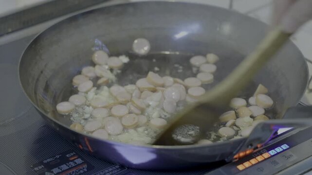 This is a scene from the process of making fried rice, where sausages and garlic are being stir-fried.